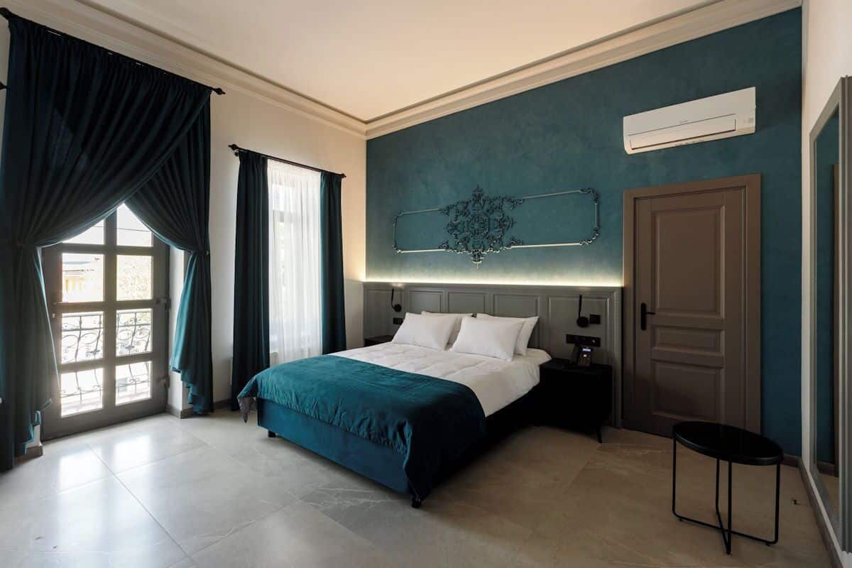 A bedroom with a bed, nightstands, a wall-mounted air conditioner, a door, and a window with curtains.
