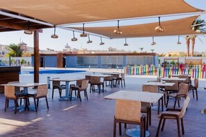 An outdoor dining area with tables and chairs, a pool, and a view of the cityscape. - A435 Comfy & Cozy in Scandic Resort with beach and pools (Hurghada)