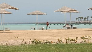 En strand med flera parasoller av halm och solstolar.