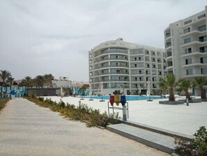A modern hotel with a pool area, palm trees, and a paved walkway. - A435 Comfy & Cozy in Scandic Resort with beach and pools (Hurghada)