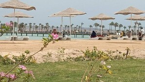 A beachside resort with lounge chairs and umbrellas, palm trees, and a pool. - A435 Comfy & Cozy in Scandic Resort with beach and pools (Hurghada)