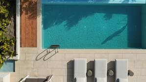 Une piscine sur le toit, avec une eau d’un bleu limpide, entourée de carreaux de couleur beige et de chaises longues blanches.