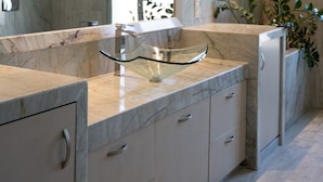 Une salle de bain moderne avec des comptoirs en marbre, un lavabo en verre et un grand miroir.