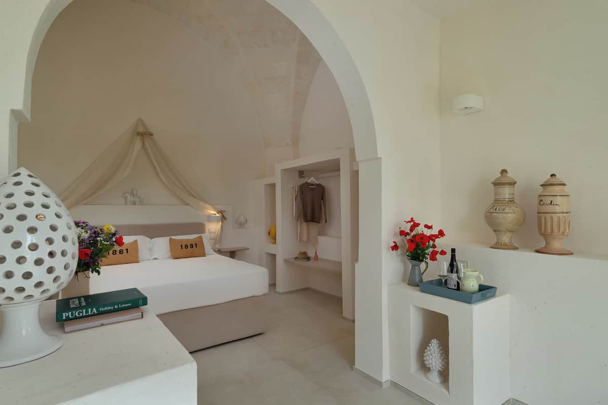 A hotel room with a bed, a nightstand, a lamp, and a vase with flowers.