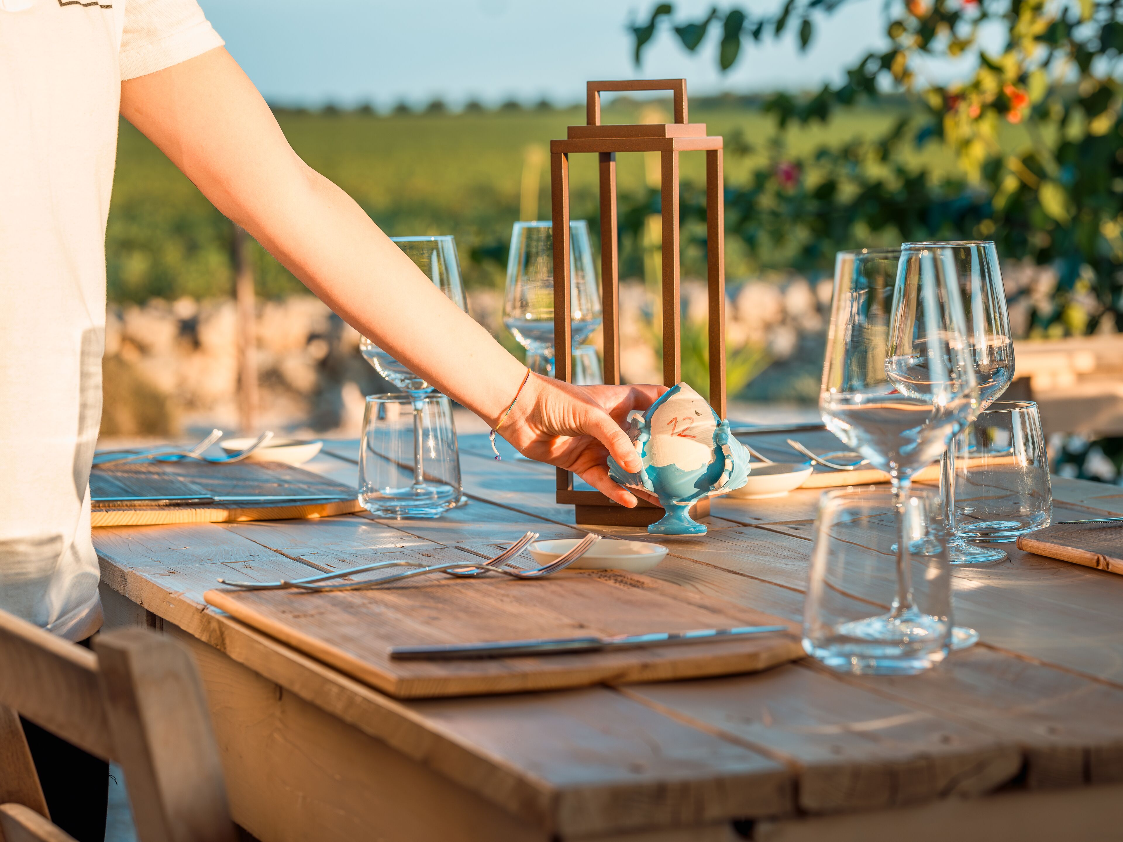 A wooden table set with wine glasses, a candle holder, and a person placing a candle in a blue holder.
