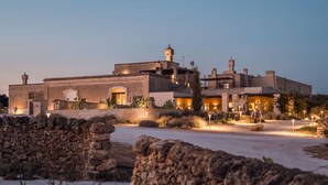 A large, multi-story building with a stone facade, multiple chimneys, and a well-lit entrance. - Masseria Cuturi (Manduria)