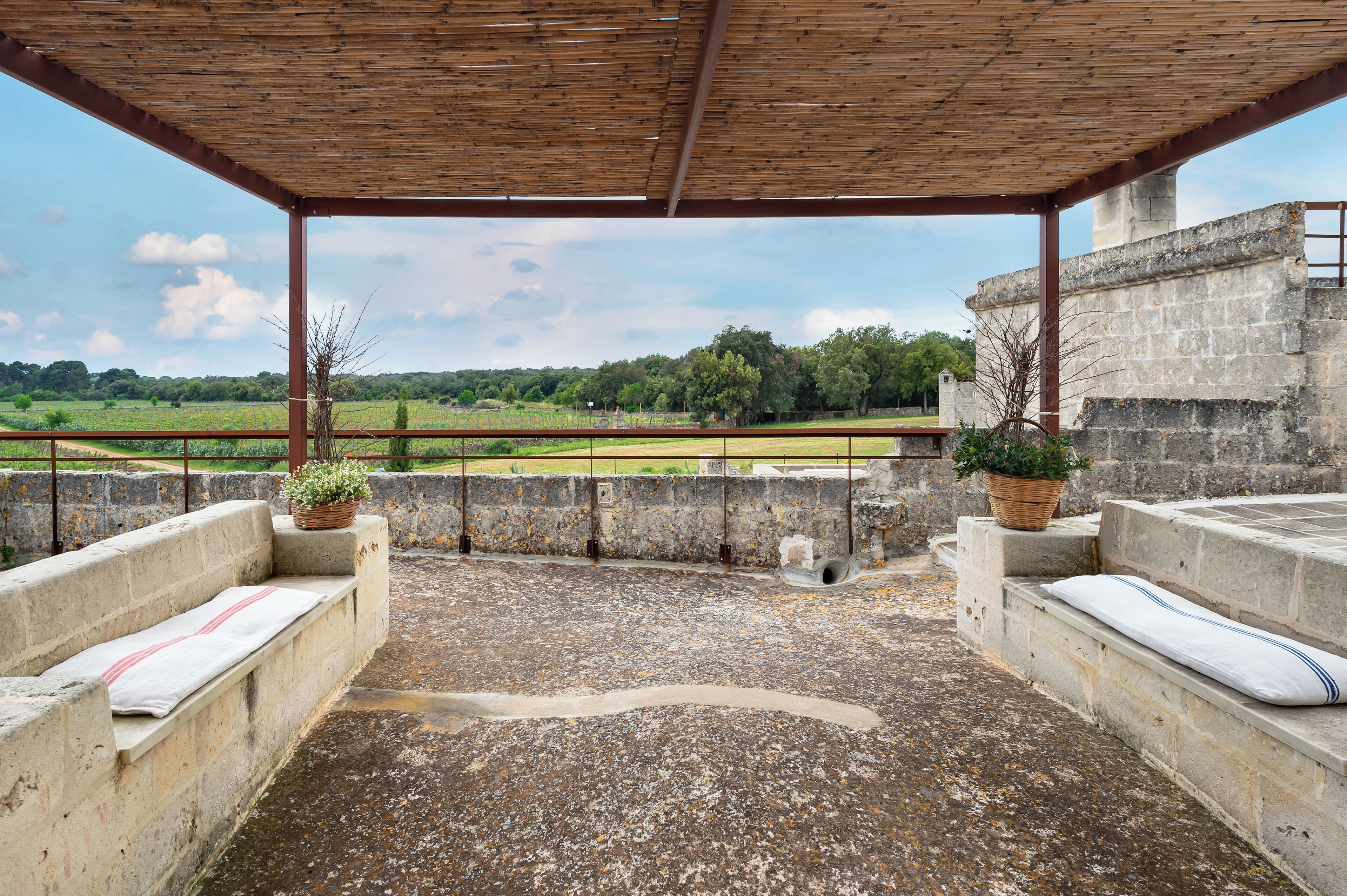 A covered outdoor area with a concrete floor, benches, and potted plants.