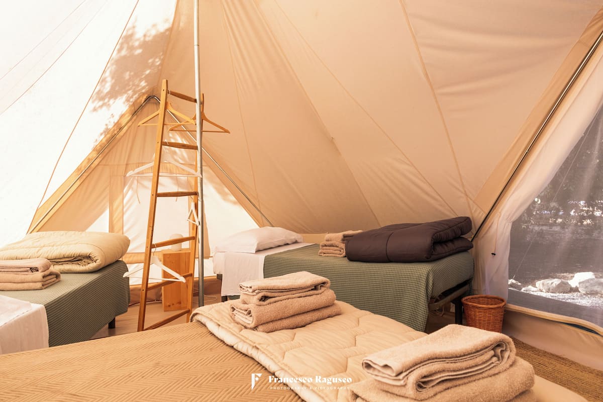A tented accommodation with two beds, a ladder, and neatly folded towels.