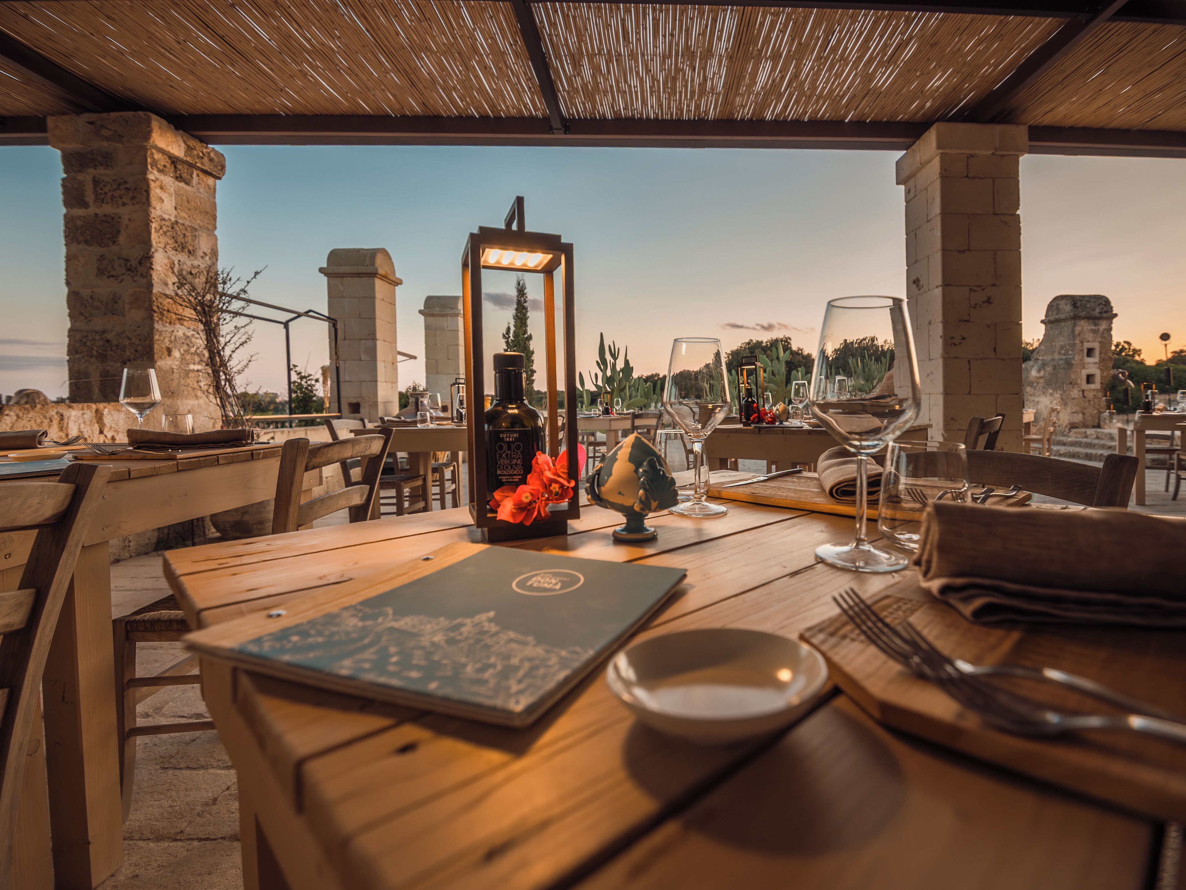 Un área de comedor al aire libre con pilares de piedra, mesas de madera y vistas a edificios históricos al fondo.