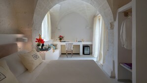A bedroom with a large bed, a desk, and a chair, connected by an arched doorway to a bathroom. - Masseria Cuturi (Manduria)
