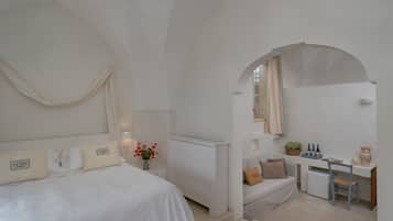 A minimalist bedroom with a bed, bedside table, and a small desk area with a chair and a plant.