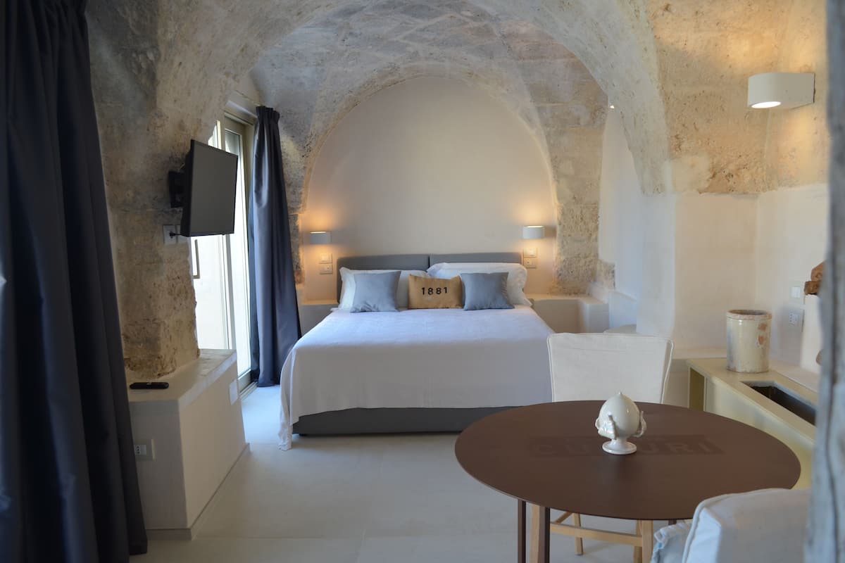 A bedroom with a stone arch ceiling, a bed with pillows, a TV, and a table with a decorative item.