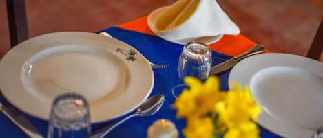 Una mesa dispuesta con platos, cubiertos, saleros y pimenteros, una copa y un jarrón con flores amarillas.