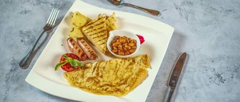 Un plato con salchichas a la parrilla, patatas asadas, un tomate a la plancha, un tazón de frijoles y una tortilla doblada.