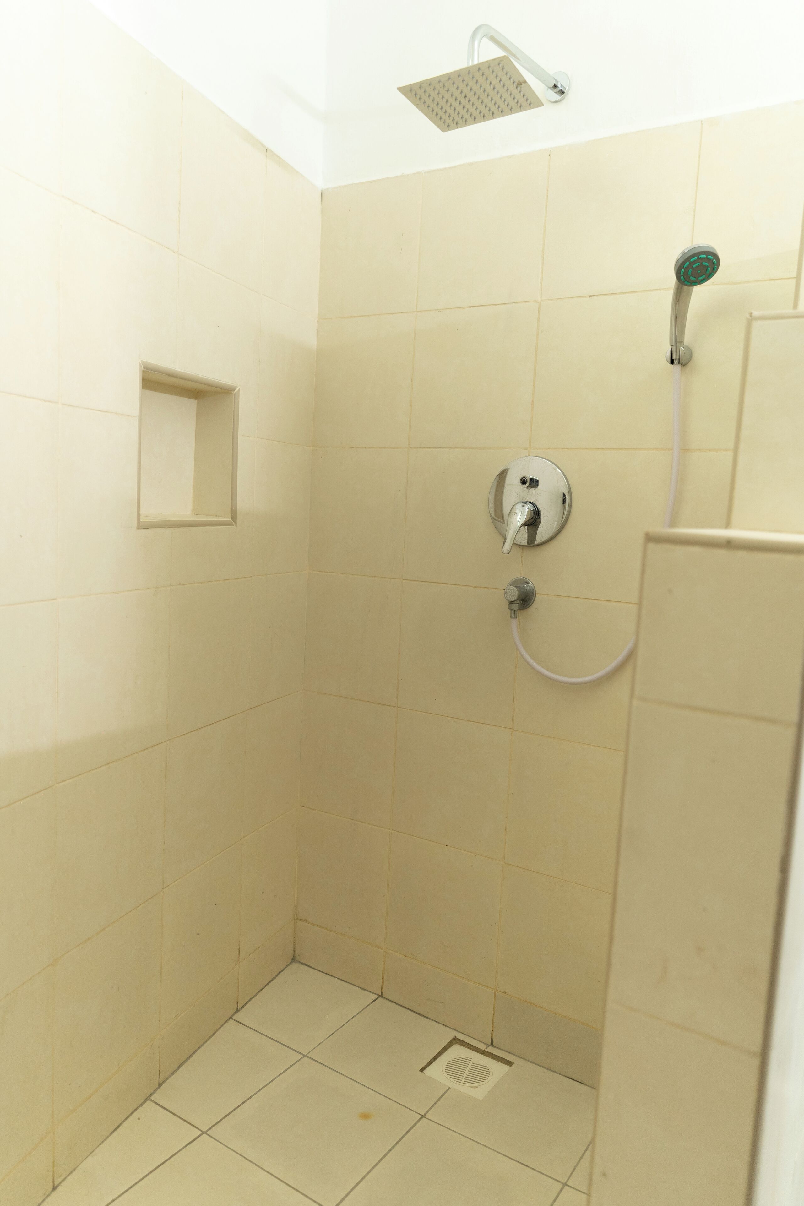 A small, tiled shower area with a handheld showerhead and a wall-mounted faucet.