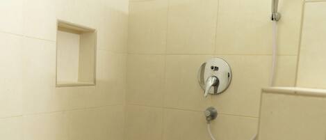 Un petit espace de douche carrelé, équipé d’un pommeau de douche à main et d’un robinet mural.