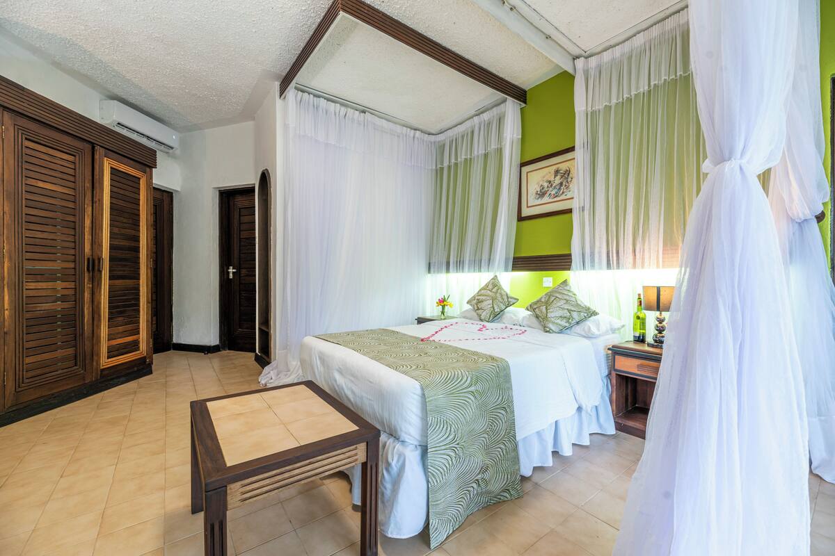 Ein Hotelzimmer mit Bett, Nachttisch, Lampe und einem Fenster mit Vorhängen.