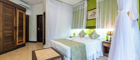 A hotel room with a bed, a bedside table, a nightstand, a lamp, and a window with curtains.