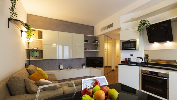 Una cocina moderna con electrodomésticos integrados, un comedor con mesa de vidrio y una sala de estar con sofá y televisor.