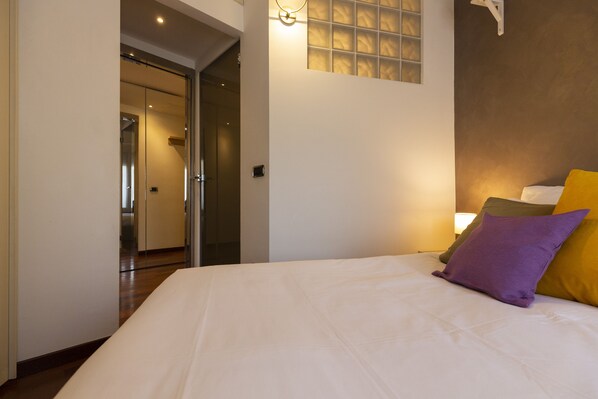A hotel room with a large bed, a nightstand, a window with blinds, and a door leading to another room. - notaMI - California Dreaming (Milan)