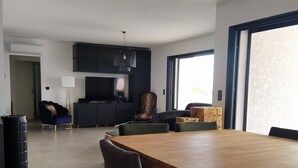 A modern living room with a wooden dining table, dark sofas, and a kitchen area in the background. - Villa Moderne Proche Solenzara (Ventiseri)