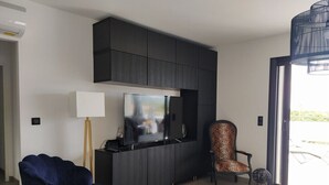 A modern living room with a dark entertainment unit, a flat-screen TV, a blue armchair, a leopard print chair, and a floor lamp. - Villa Moderne Proche Solenzara (Ventiseri)