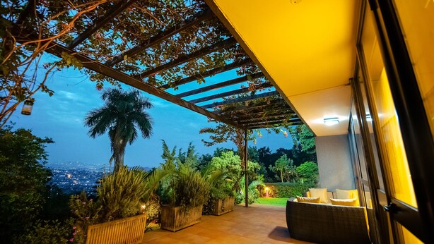 An outdoor patio area with a pergola, potted plants, and a seating area with cushions. - Pangolin Nest Boutique Hotel (Kampala)