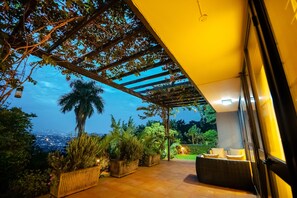 Area patio esterna con pergola, piante in vaso e zona salotto con cuscini.