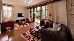 A spacious living room with a large TV, comfortable seating, and a view through the glass doors. - Pangolin Nest Boutique Hotel (Kampala)
