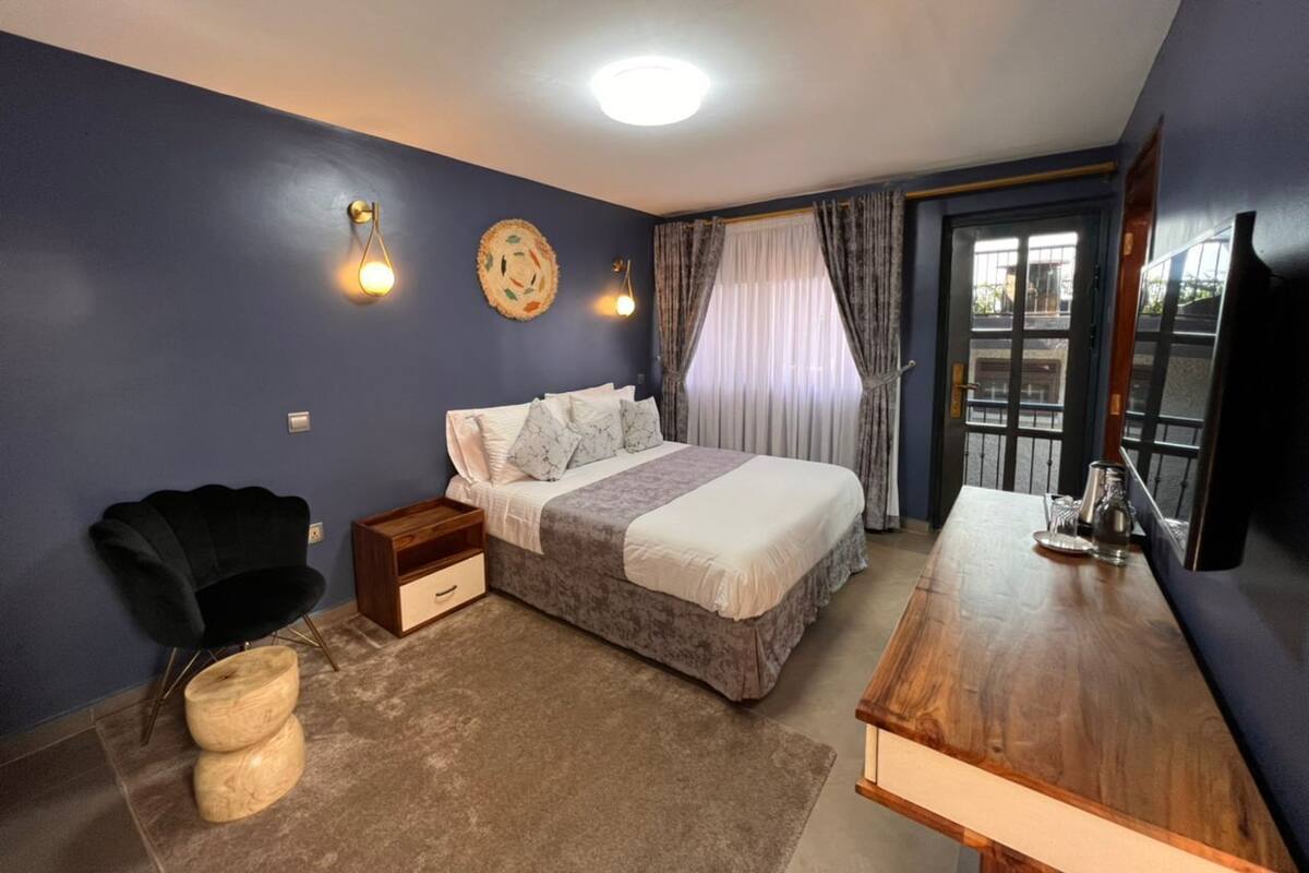 Um quarto com cama, mesas de cabeceira, uma cadeira, escrivaninha e televisão.