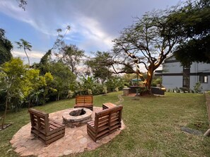 A backyard with a fire pit, wooden benches, and a large tree.