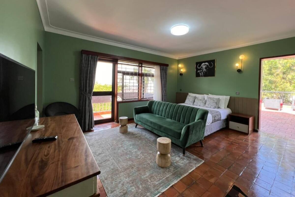Quarto com sofá verde, cama, televisão e porta de vidro deslizante para área externa.