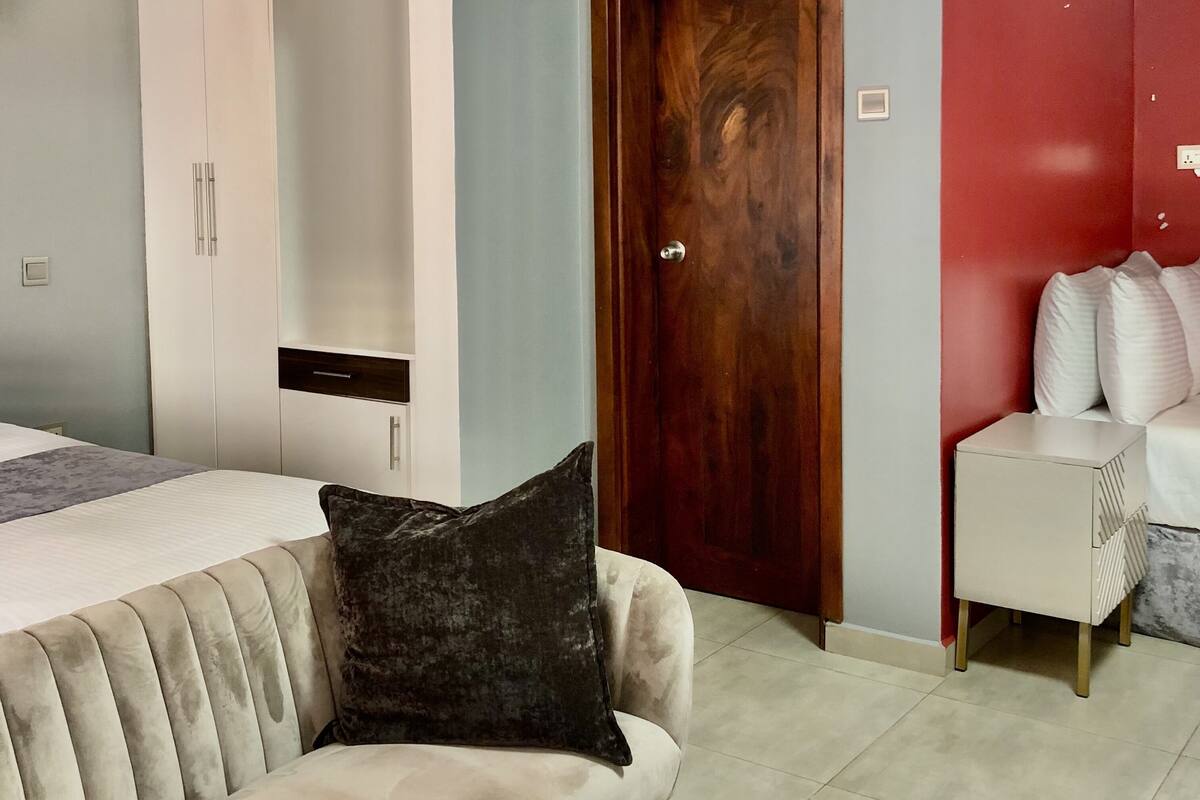Um quarto com cama, guarda-roupa, porta, sofá e mesa de cabeceira.
