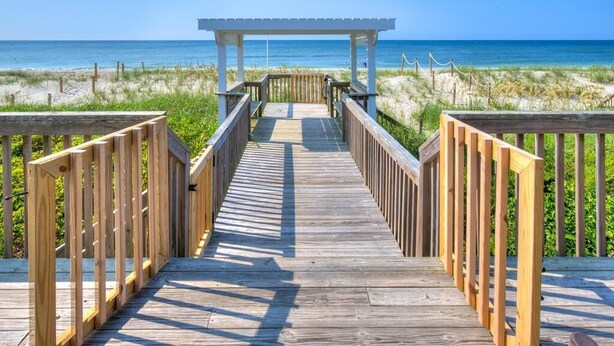 A wooden boardwalk leading to a beach with a white pergola structure. - Enjoy a spacious oceanfront duplex at Codfather Unit 2 (Oak Island)