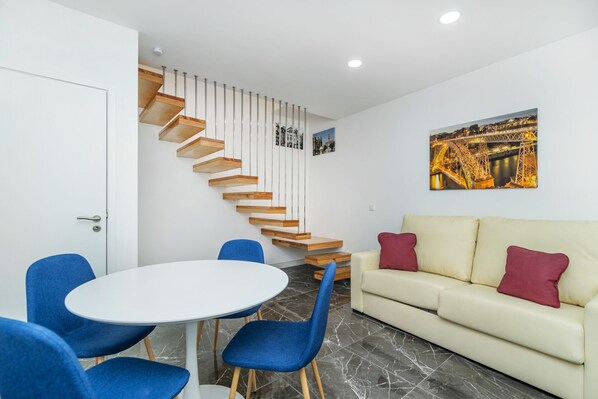 A modern living room with a white sofa, blue chairs, a round table, a wooden staircase, and a cityscape painting. - MAREDIMO VILLAGE (Porto)