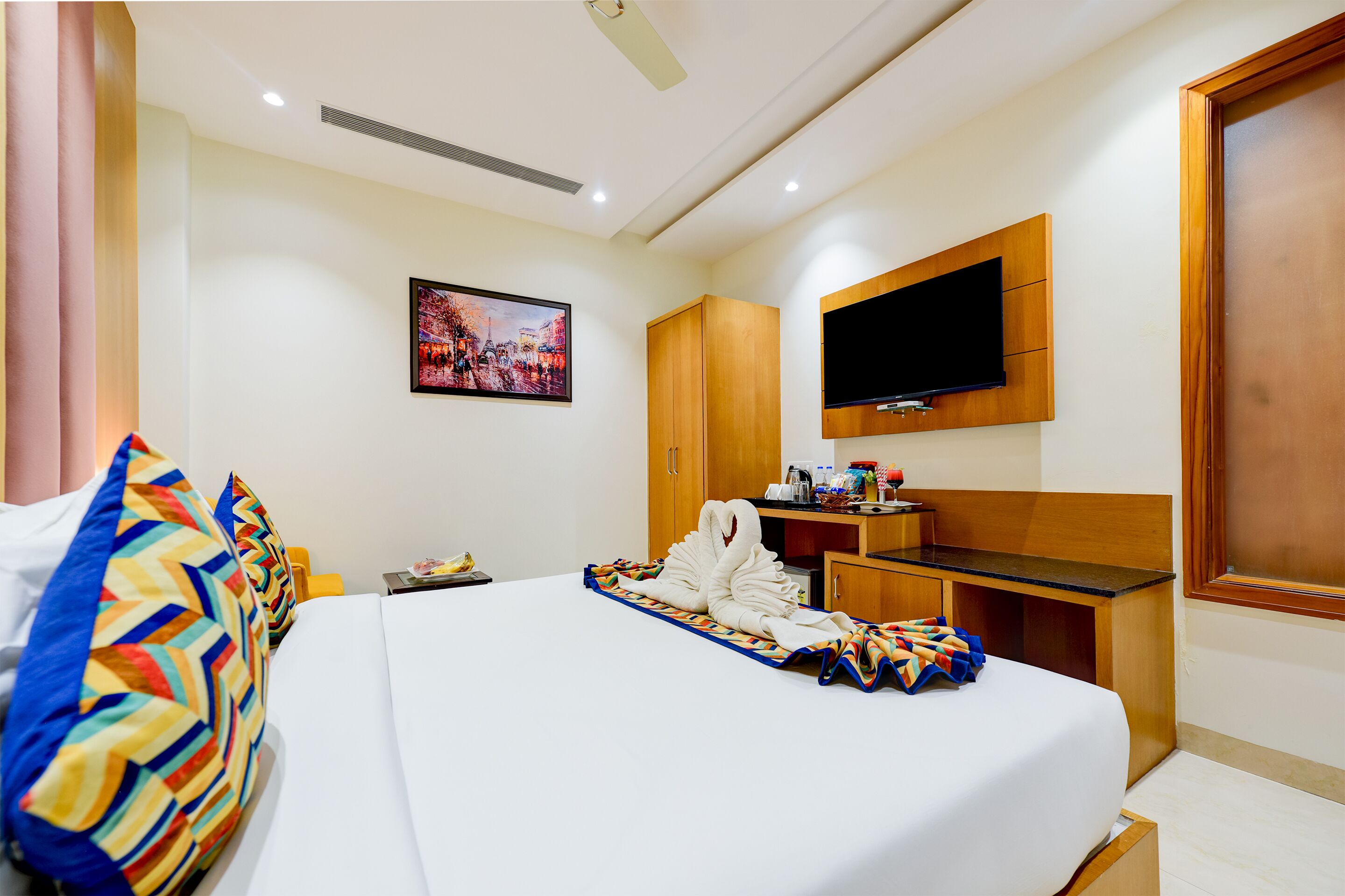 A hotel room with a bed, a desk, a television, and a wall-mounted TV.