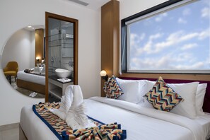 Une chambre d’hôtel avec un lit, un grand miroir, une salle de bain avec un lavabo et une fenêtre donnant sur le ciel.