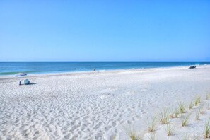 A sandy beach with a few people, a blue umbrella, and a small boat in the distance.