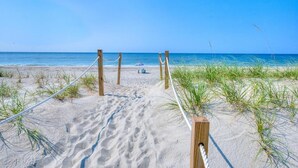 A sandy beach path leading to the ocean with a rope barrier and a single umbrella. - Oceanfront Codfather Unit 1, a spacious 3-bedroom duplex in Oak Island. (Oak Island)