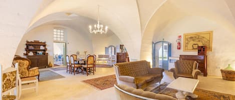 A spacious loft with high ceilings, a chandelier, a dining area with chairs and a table, and a cozy seating area with a sofa and armchairs.