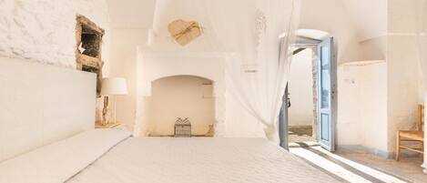 A spacious bedroom with a large bed, a wooden chair, and a small table with a lamp.