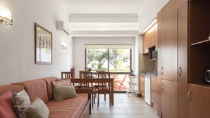 A modern kitchen with wooden cabinets, a dining area with a table and chairs, and a sofa with cushions. - Alvaflor 102 - Vilamoura by HD Properties (Vilamoura)