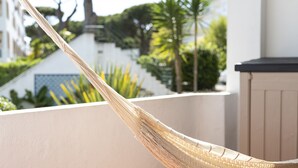 A hammock on a balcony with a view of a white building and greenery. - Alvaflor 102 - Vilamoura by HD Properties (Vilamoura)
