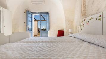 A bedroom with a large bed, a red chair, a white wall with a floral design, and an open door leading to a balcony.