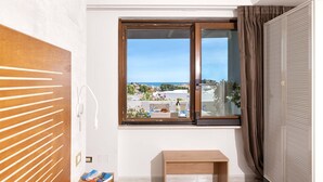 A room with a wooden door, a window with a view of the sea, a small wooden table, and a power outlet. - 3365 A Casa di Anna - Ilaria by Barbarhouse (Vieste)