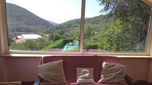 Une pièce dotée d’une grande fenêtre donnant sur un paysage verdoyant et une piscine.