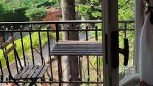 Un balcon avec une table et des chaises en bois, donnant sur un paysage verdoyant et luxuriant.