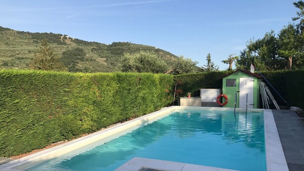 A swimming pool with a clear blue water, surrounded by a stone deck. There is a small shed with a flag on top, and a hedge in the background. - Large apartment with pool and garden, ideal for families, 10 km from the sea. (Sarola)
