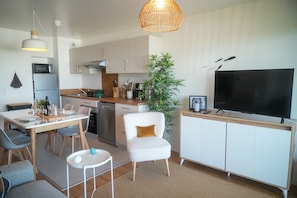 A modern kitchen with a dining area, a TV, and a large plant.
