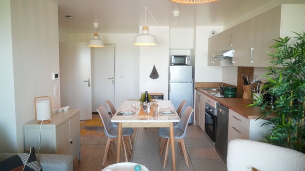 Una cocina moderna con armarios blancos, una mesa de comedor con sillas y una lámpara colgante.
